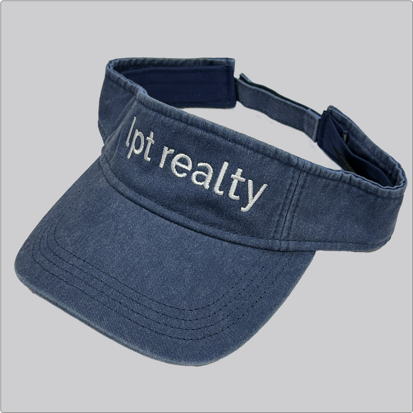 A casual, washed denim visor in blue with “lpt realty” embroidered in white across the crown.
