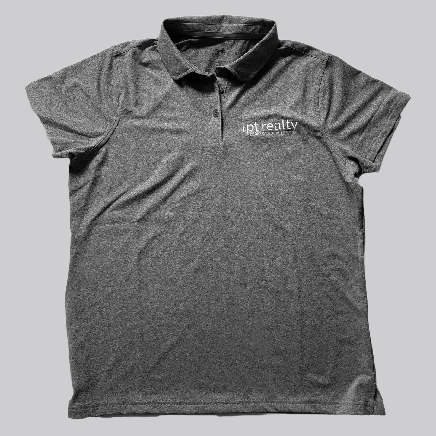 A heathered dark gray polo shirt with a subtle sheen from the stretch fabric. The upper left chest features “lpt realty” in white, embroidered lowercase letters, with “BROKERAGE FOR LIFE” in smaller, all caps beneath it. The shirt’s placket has 3 buttons in matching gray, the collar is the same fabric as the shirt, and the sleeves are open with no cuffs.