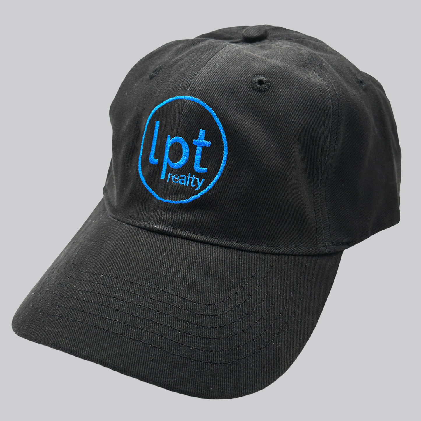 A black twill cap with a relaxed fit, matching stitching, and embroidered eyelets. The front panels feature the “lpt realty” circle logo embroidered in sky blue. 