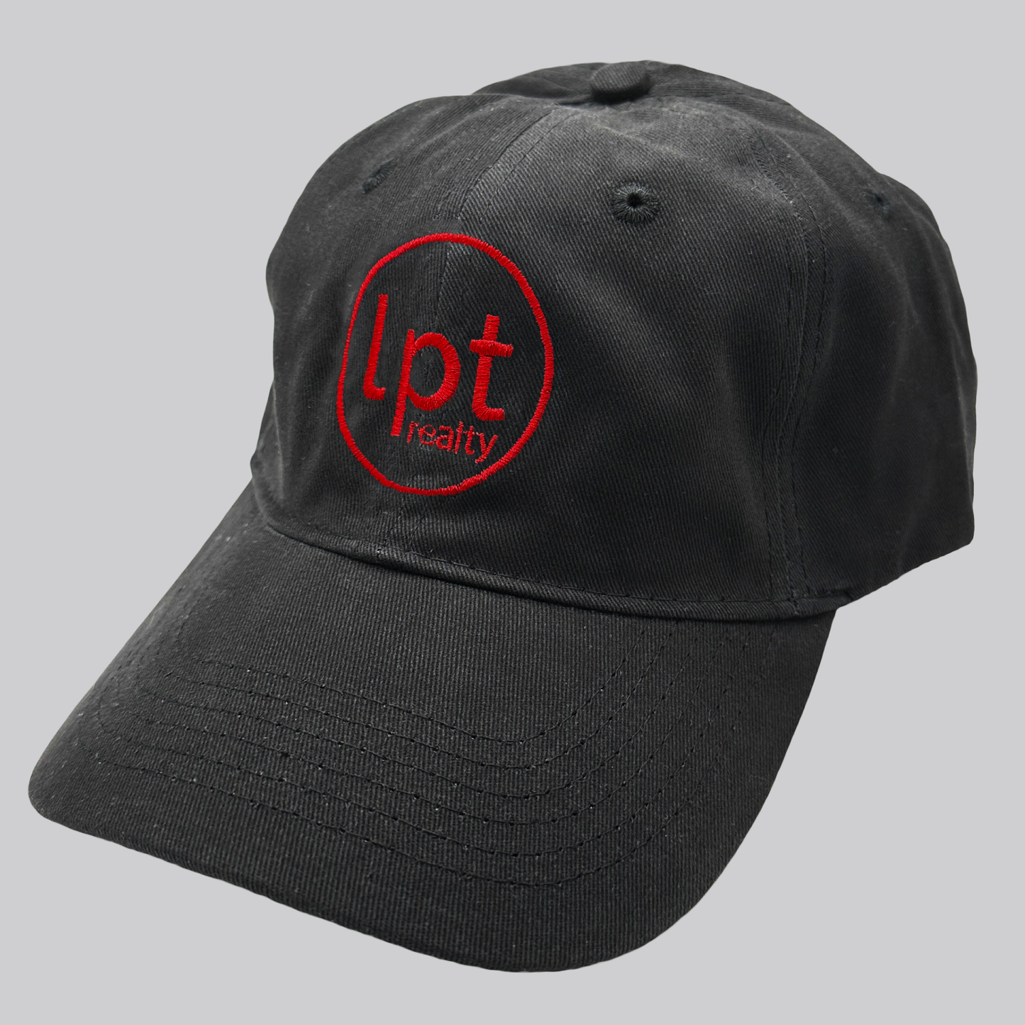 A black twill cap with a relaxed fit, matching stitching, and embroidered eyelets. The front panels feature the “lpt realty” circle logo embroidered in bright red. 