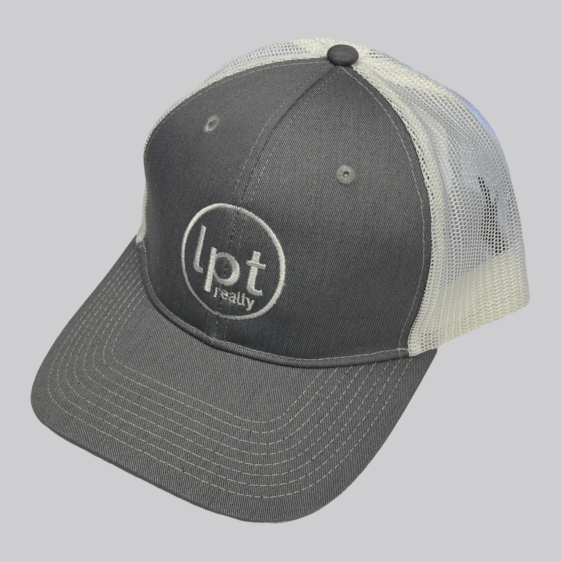 Classic two-toned trucker hat design with solid front panels and white mesh back. The front panels and bill are a medium heather gray with matching embroidered eyelets, an embroidered white “Lpt Realty” circle logo at the center, and white stitching on the bill. 