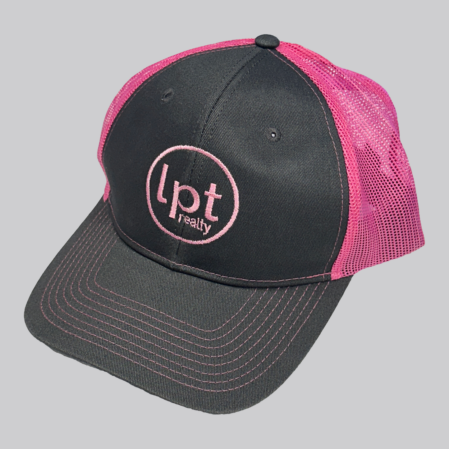 Classic two-toned trucker hat design with solid front panels and neon pink mesh back. The front panels and bill are a solid graphite gray with matching embroidered eyelets, an embroidered neon pink “Lpt Realty” circle logo at the center, and neon pink stitching on the bill. 