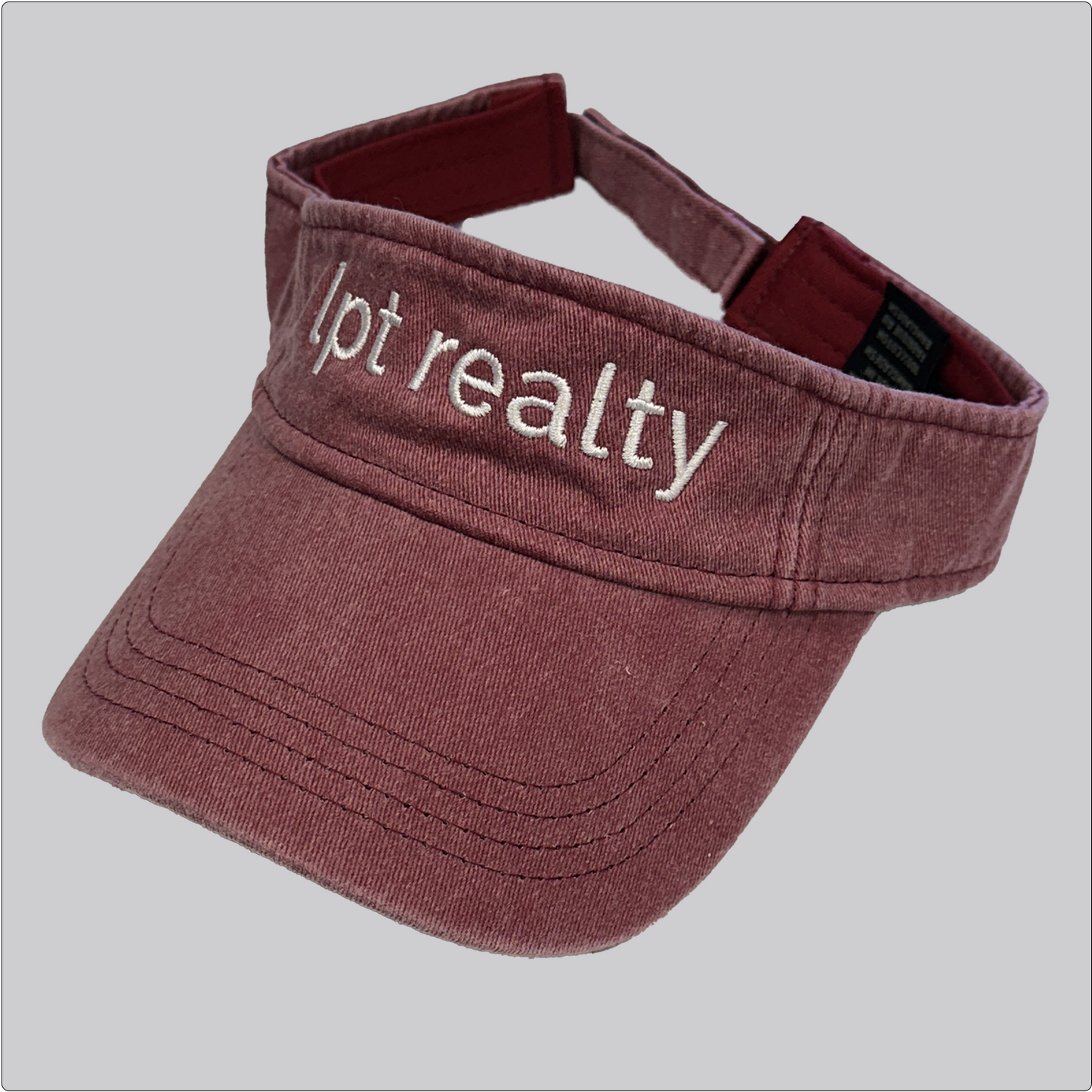 A casual, washed denim visor in brick red with “lpt realty” embroidered in white across the crown. 