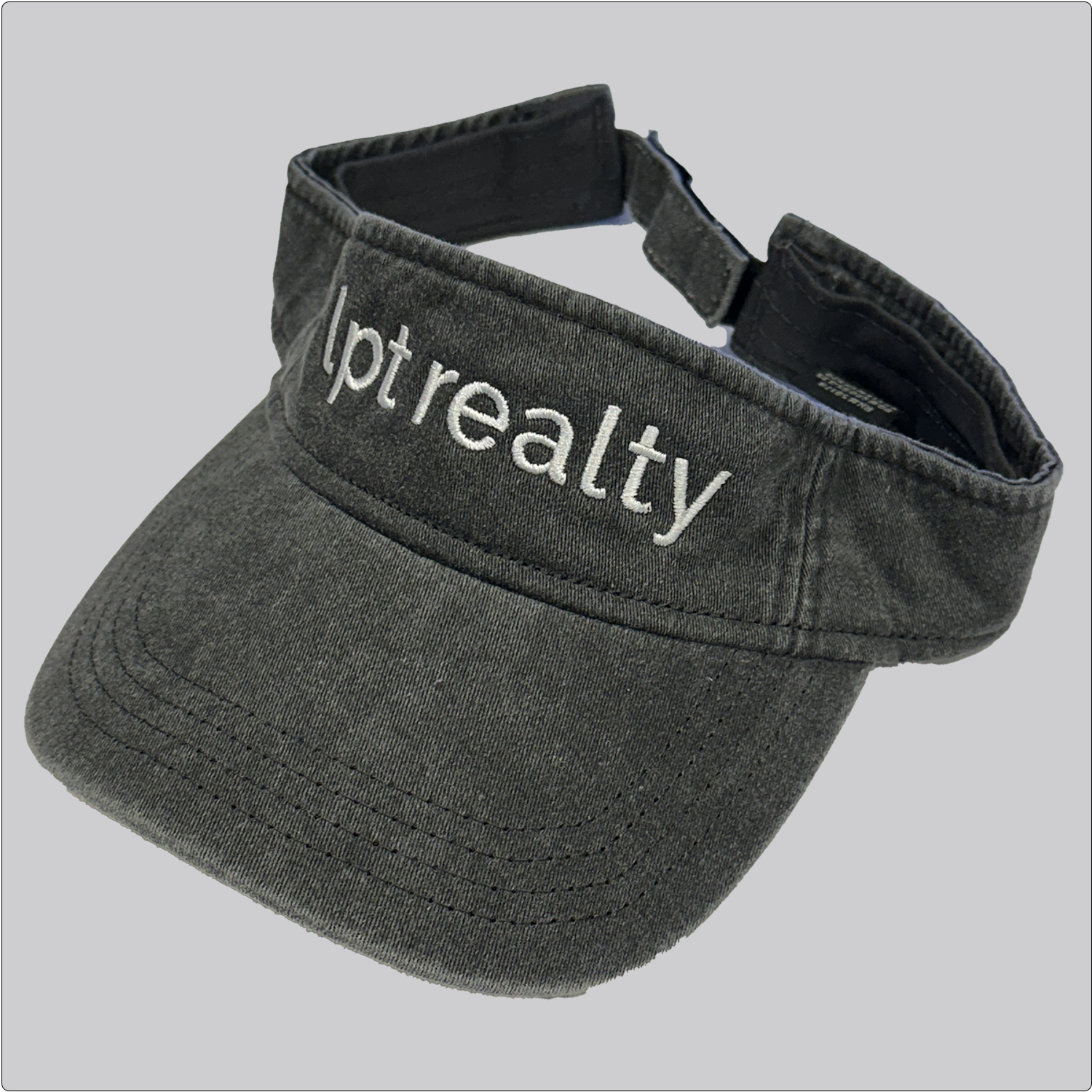 A casual, washed denim visor in black with “lpt realty” embroidered in white across the crown. 