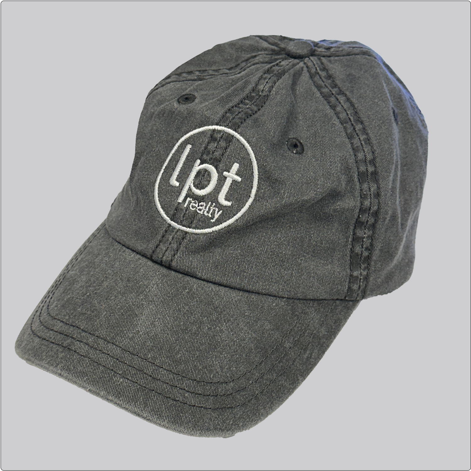 A casual, washed denim cap in a charcoal black with the “lpt realty” circle logo embroidered in white across the front panels. Stitching and embroidered eyelets are in matching black thread. 