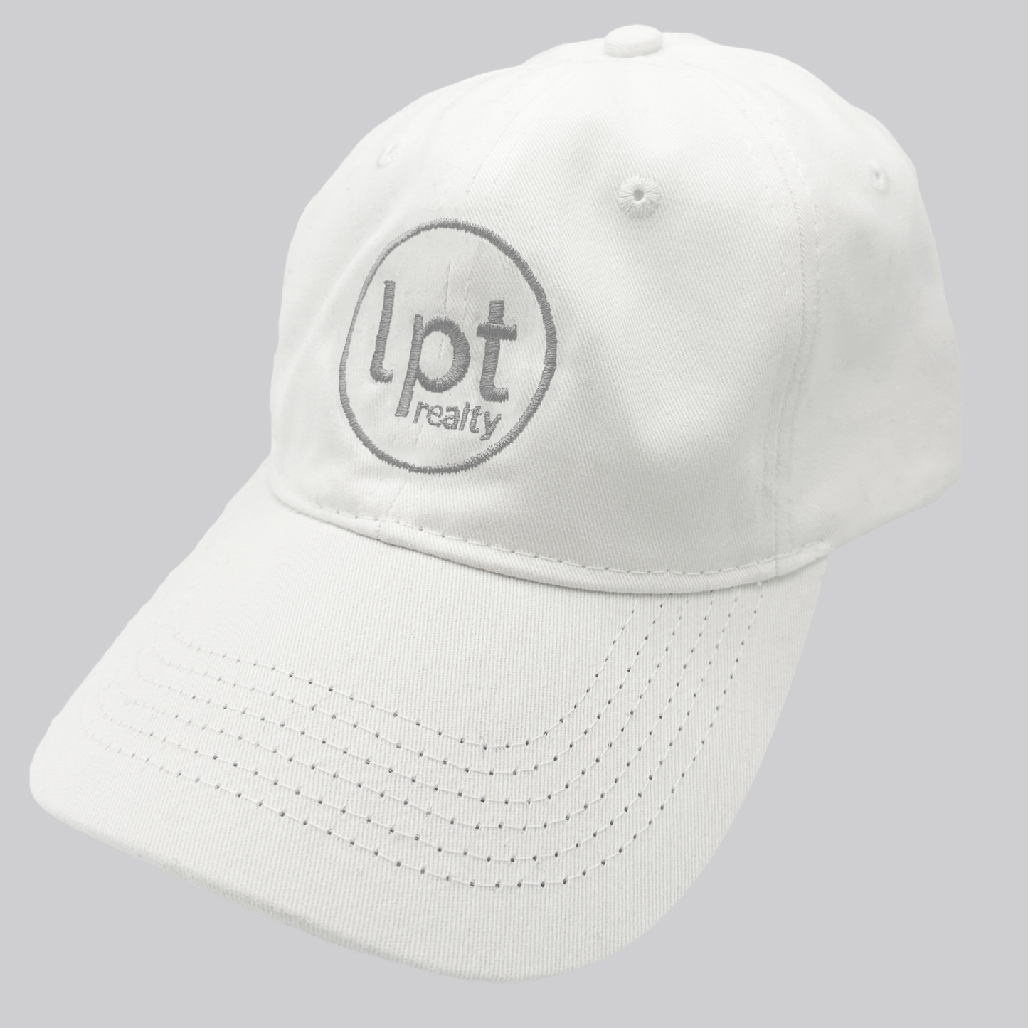 A white twill cap with a relaxed fit, matching stitching, and embroidered eyelets. The front panels feature the “lpt realty” circle logo embroidered in silver. 