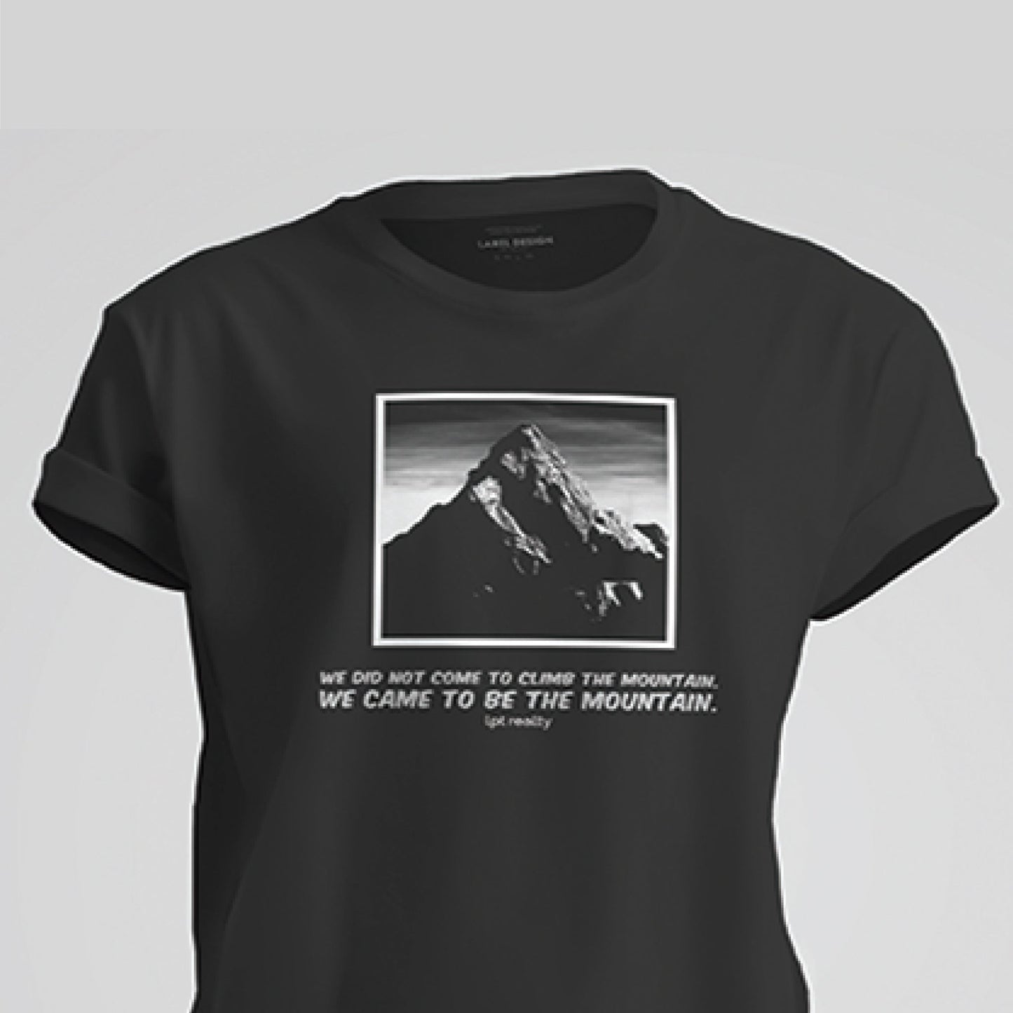 A black, short-sleeved t-shirt featuring a grayscale image of a large mountain surrounded by a white border. Two lines of white, capitalized text under the image read, with the second in larger font than the first: “ We did not come to climb the mountain. We came to be the mountain.” Below the text, in white, lowercase letters, it reads “lpt realty.” On the back, a few inches below the neckline, is the LPT circle logo. 